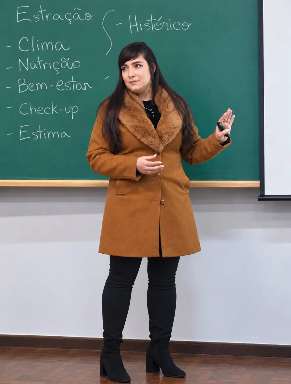 Dra Tay palestrando em sala de aula, com um quadro escrito ao fundo
